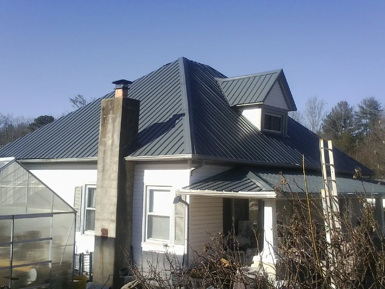 Dark blue standing seam metal roof on a white farmhouse with dormer — Slate & Tile Roof Repair by Roofing Brothers in Quitman