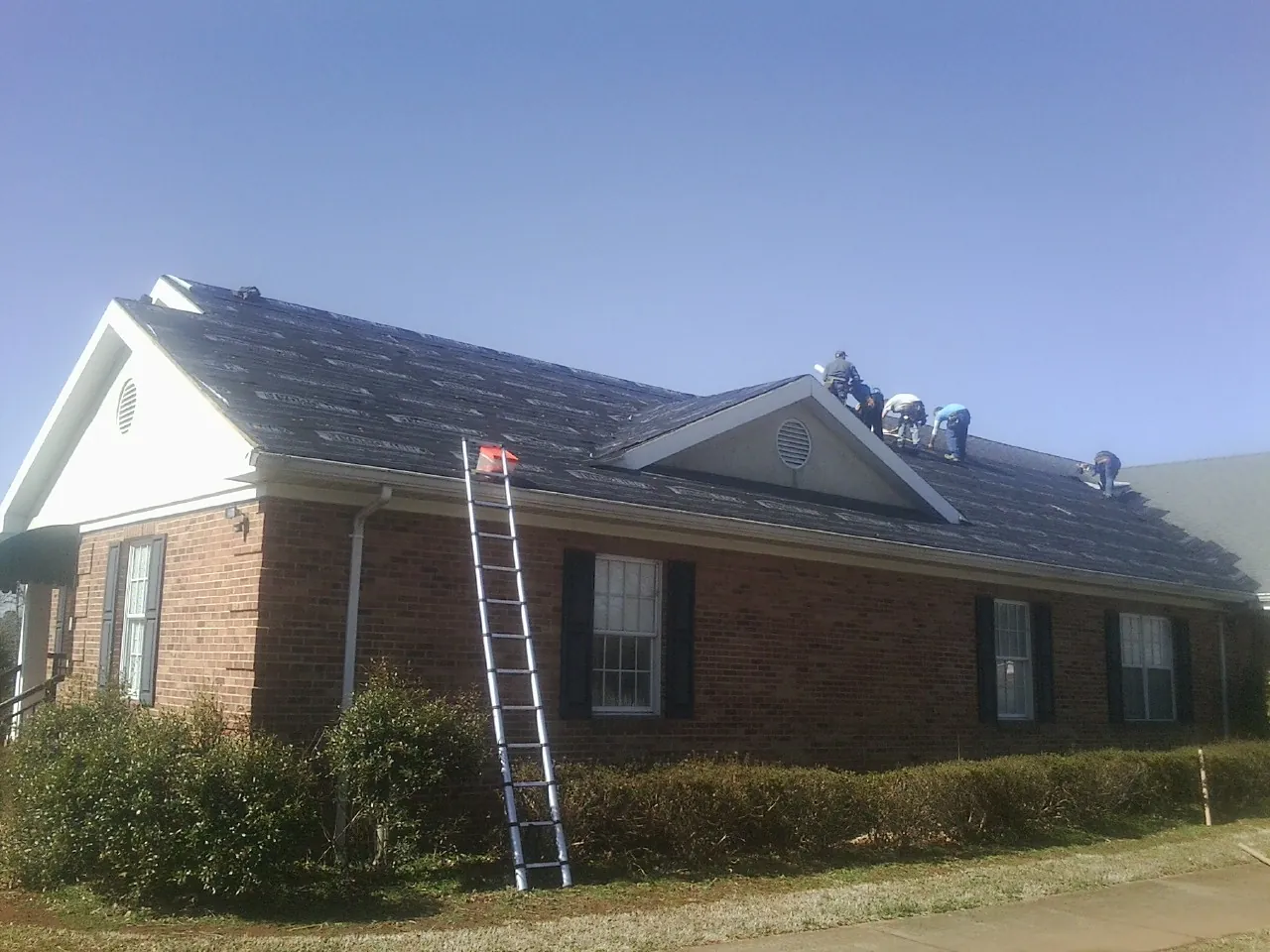 Crew tearing shingles off a brick ranch roof with a ladder set — Metal Roof Repair work by our crew in Quitman