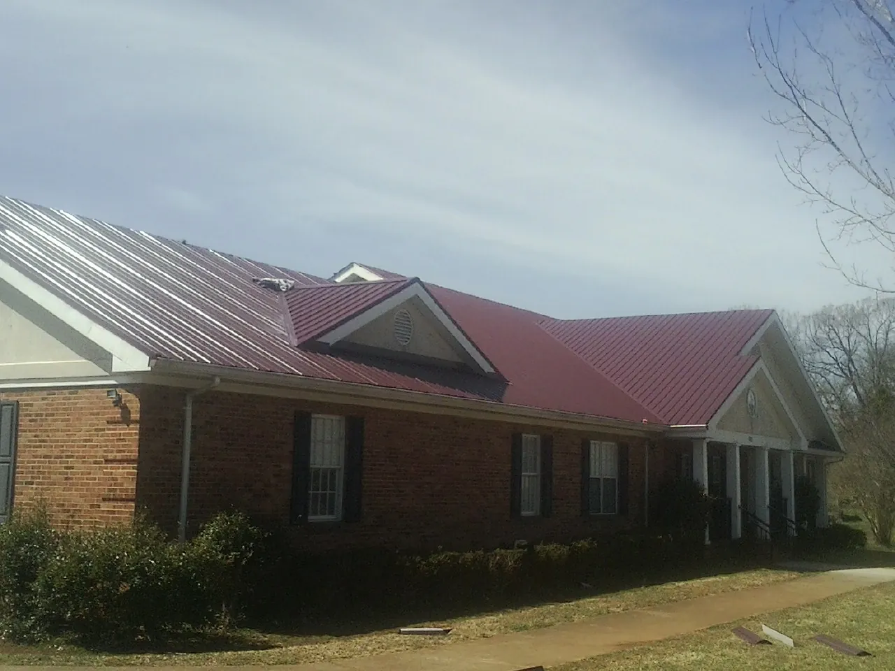 Red metal roof with gabled entries on a long brick building, from a Hail Damage Roof Repair job in Quitman