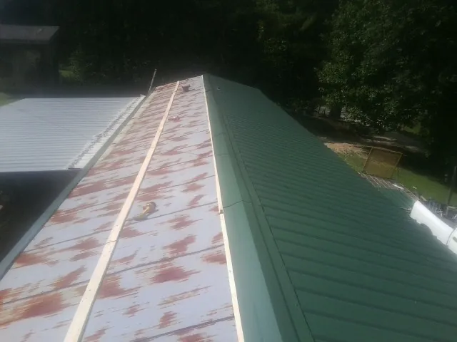Old rusted panels beside newly installed green metal roofing — Wind Damage Roof Repair by Roofing Brothers in Quitman