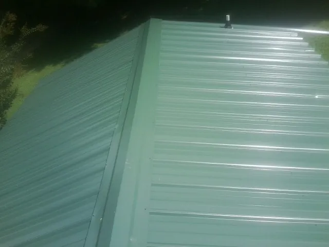 New green metal panels meeting at the ridge of a roof — Flat Roof Repair work by our crew in Quitman