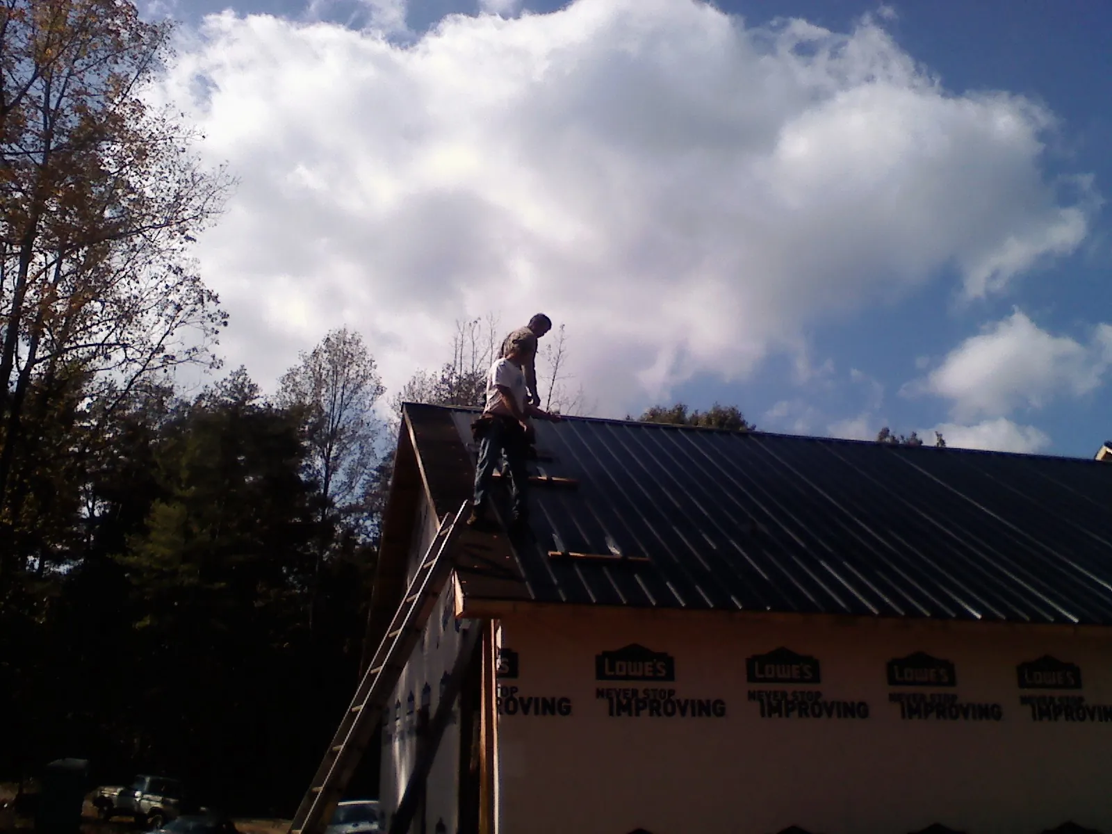 Roofer fastening dark metal panels high against a cloudy sky in Quitman