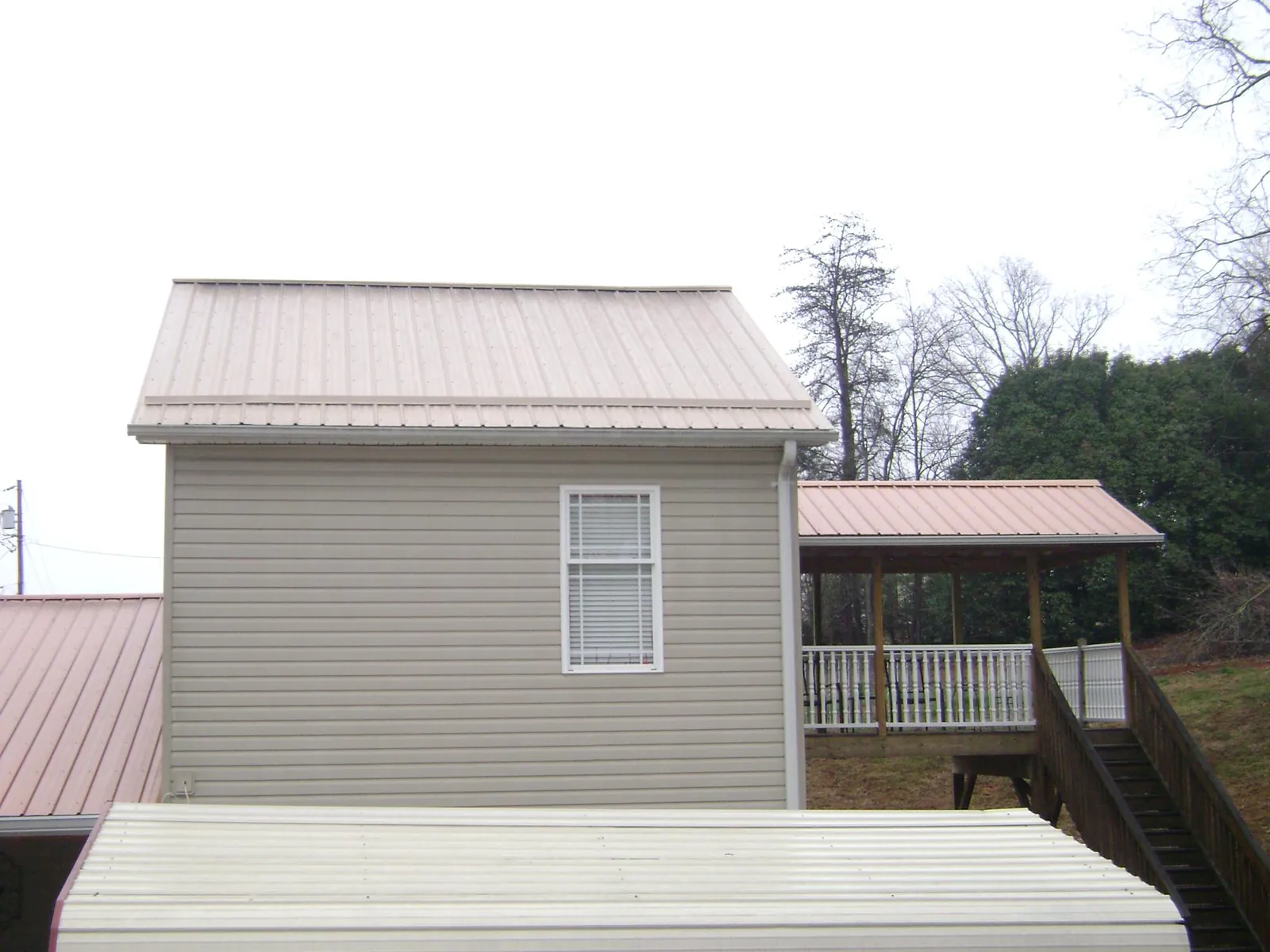 Tan metal roofs on a two story addition and attached porch, from a Roof Replacement job in Quitman